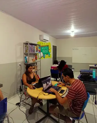 Alunos em aula prática de informática usando notebooks em mesas redondas